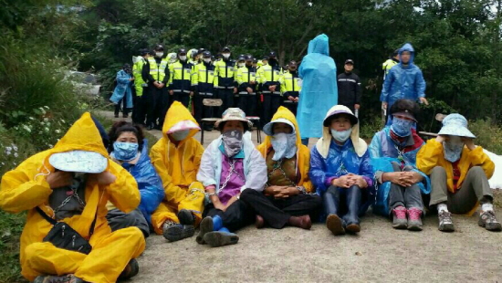 오전 9시 37분 현재 밀양시 단장면 바드리 89번 현장에는 쇠사슬로 몸을 묶고 서로를 연결한 체 밤을 새운 바드리 주민 9명과 문정선 밀양시의원이 경찰과 대치하고 있다