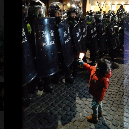 부모의 손을 잡고 청계광장으로 이동하던 어린이가 청계천 모전교 앞에서 방어막을 치고 시민들을 통제하는 경찰 앞으로 다가가 촛불을 들어 올리고 있다. ©이종식