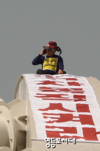 25일 오전 마포구 양화대교 아치형 철탑 위에서 “해고자를 복직시키라”는 현수막을 펼쳐놓고 농성을 벌이고 있는 김정근(60세) 씨가 누군가와 전화통화를 하고 있다. &copy;영등포시대 